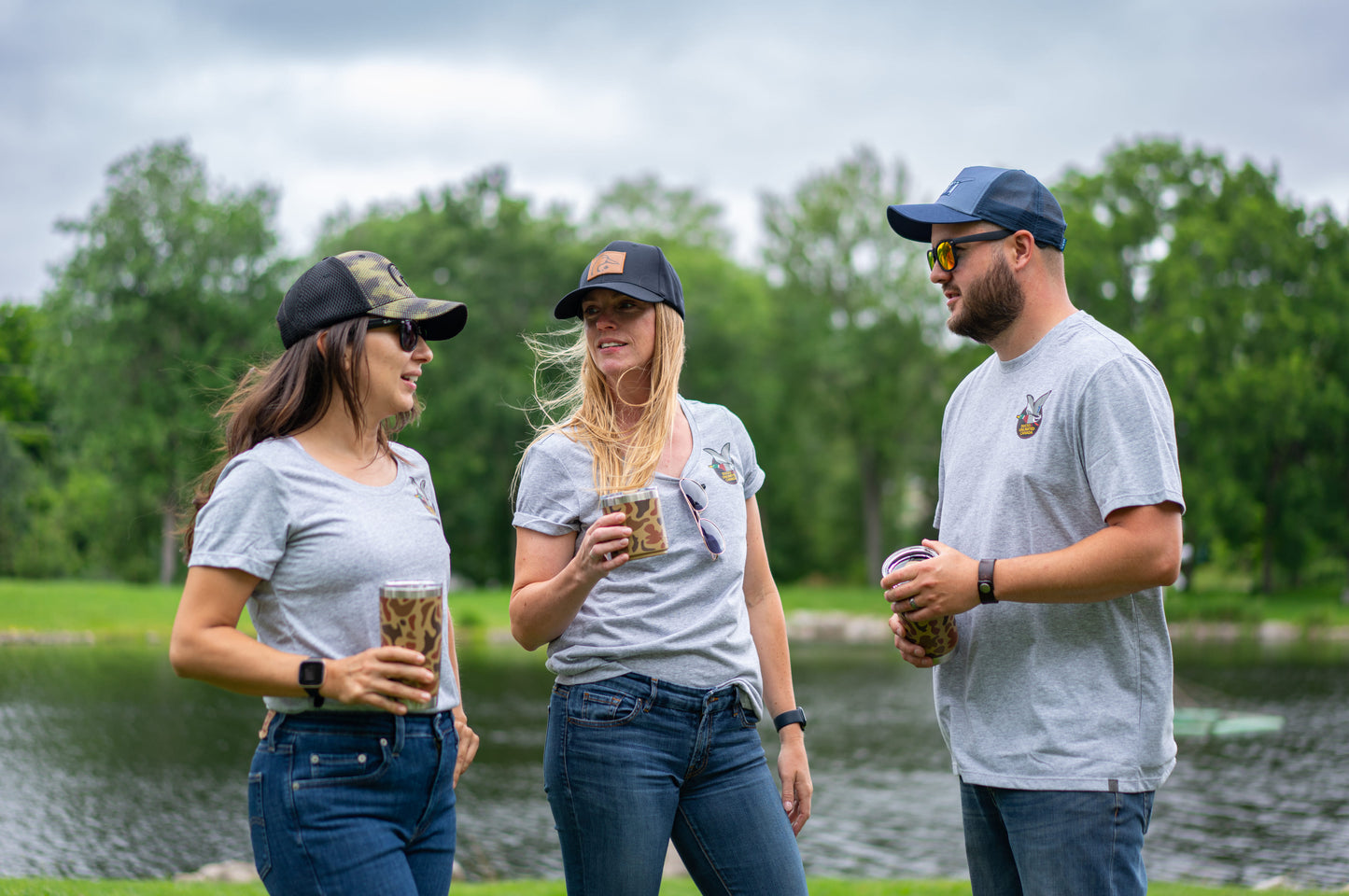 Three people wearing matching gray t-shirts with a DUCS logo, standing by a lake.